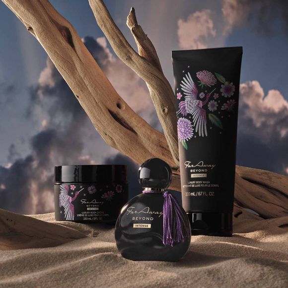 Far Away Beyond Body Creme, Eau de Parfum Spray and Body Lotion on sand with driftwood and clouds