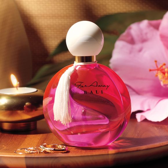 Bottle of Far Away Bali perfume on table with candle, flower and rings
